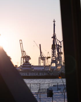Silhouette of cranes in Hamburg's harbor against a sunset sky, creating a dramatic industrial scene.