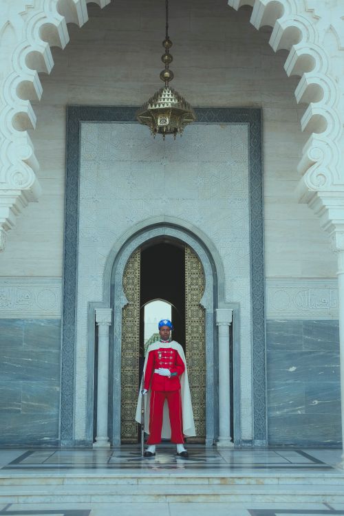 Free Moroccan royal guard in traditional attire stands at an ornate historical doorway in Rabat. Stock Photo