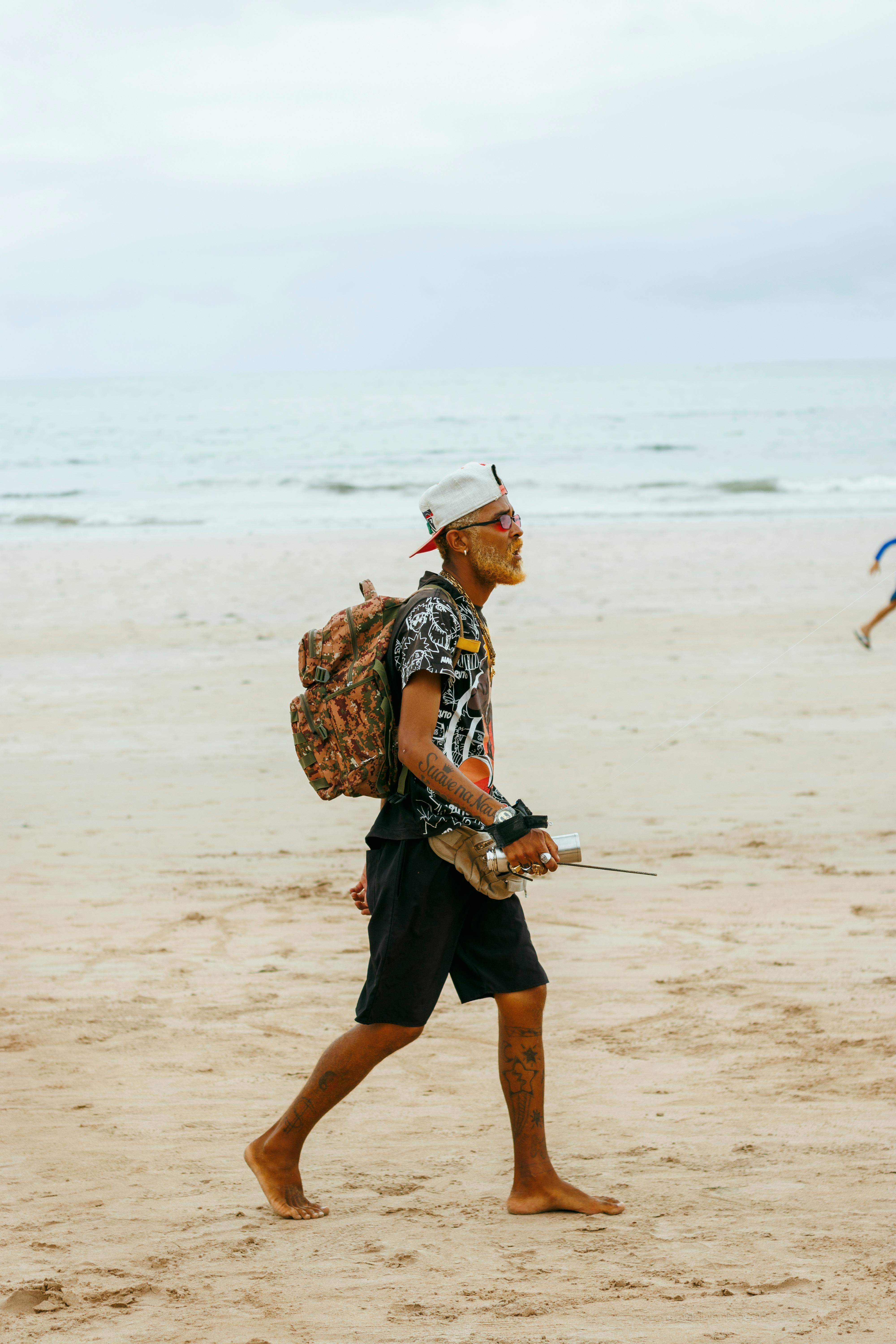 person walking barefoot on sandy beach with backpack