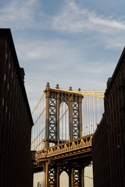 Free A view of the Manhattan Bridge captured between buildings in Brooklyn, New York at dusk. Stock Photo