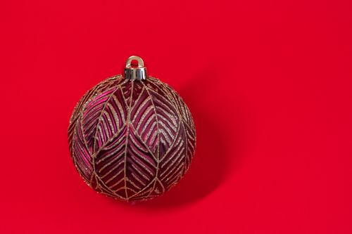 Free A single decorative Christmas ornament with gold patterns on a vibrant red background. Stock Photo