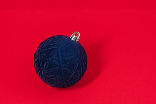 Free Navy blue Christmas ornament against a vibrant red backdrop, perfect for festive decor. Stock Photo