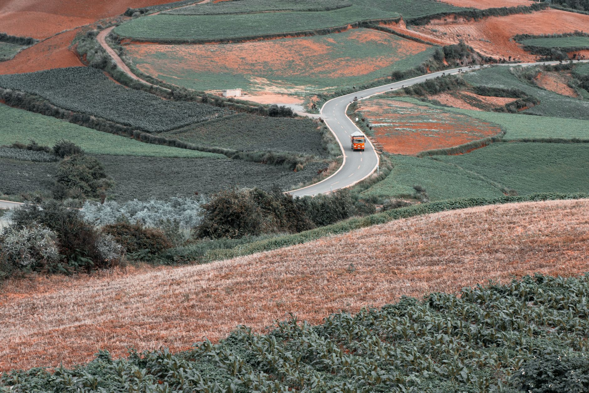 A winding road through colorful autumn fields with a vehicle traveling along its path.