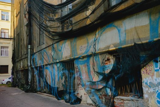 A dilapidated urban wall covered in colorful graffiti and netting, showcasing street art.