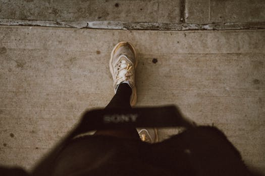 View from above of a person walking on a concrete sidewalk in urban setting wearing sneakers.