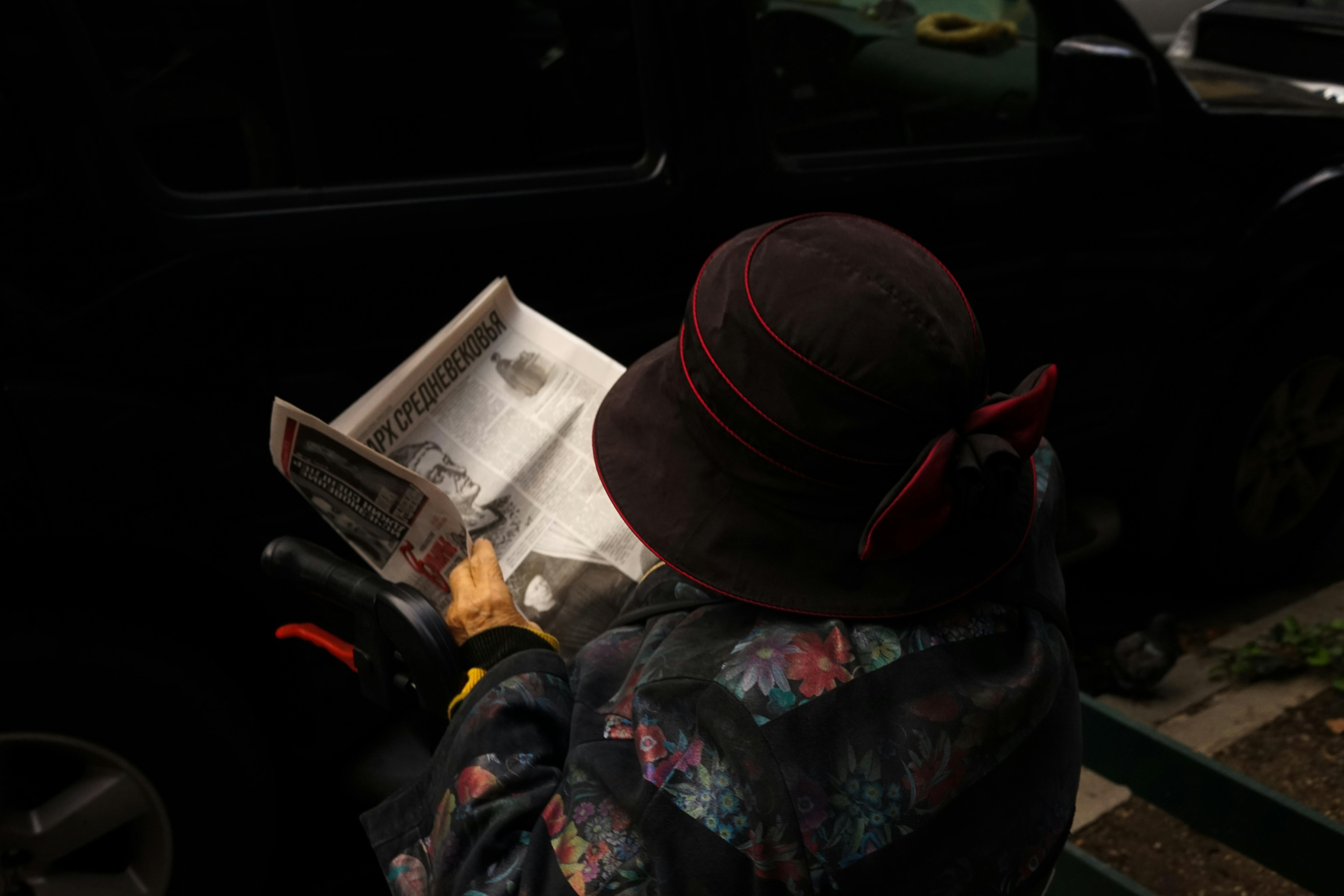 elderly woman reading newspaper outdoors