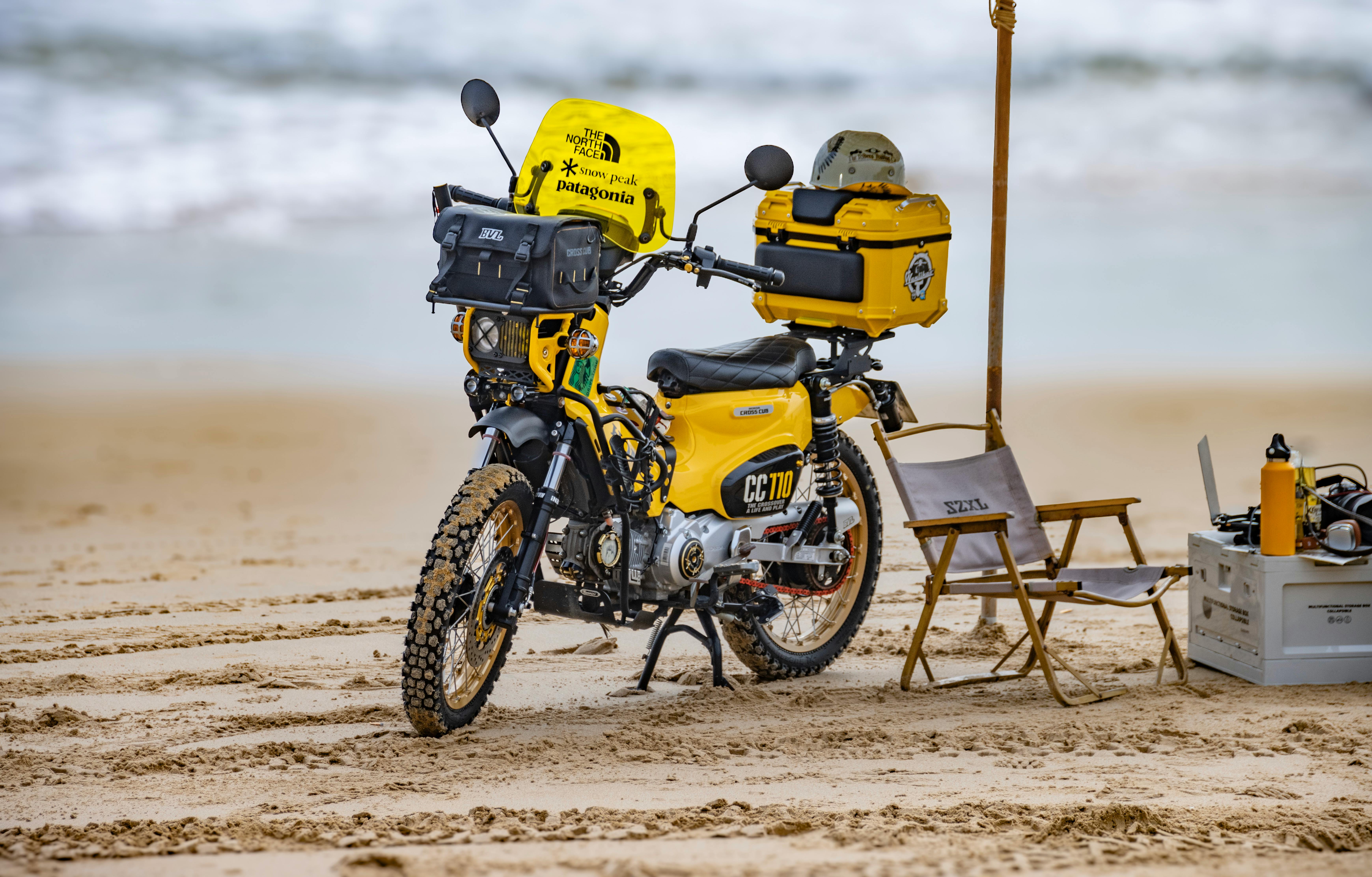 Adventure motorcycle parked on sandy beach with camping gear setup.