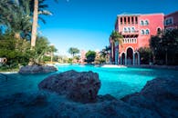 在阳光明媚的日子里，度假村池畔区域种植着棕榈树，并建有充满活力的红色建筑，令人惊叹