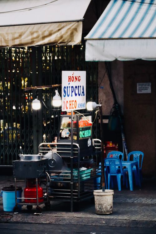 Free A vibrant Vietnamese street food stall setup with bold signs and blue chairs on a city street. Stock Photo