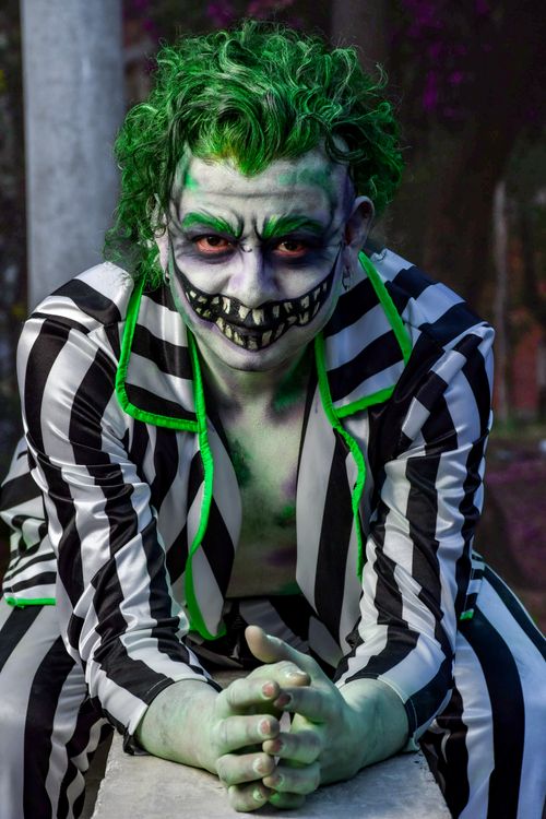 Free Green-haired cosplayer in black and white stripes posing outdoors, vivid makeup. Stock Photo