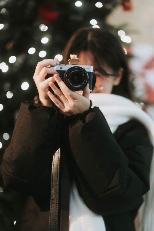 Free Young woman taking a photo with a camera outdoors, surrounded by festive lights. Stock Photo