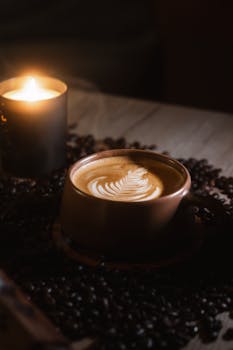 Warm coffee cup with latte art and candlelight on rustic table, creating a calm, relaxing atmosphere.