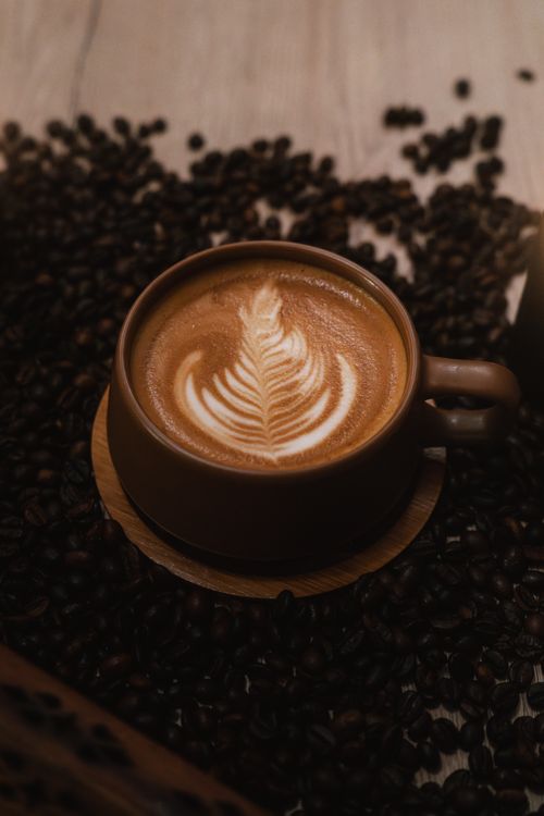 Free Warm latte with leaf design surrounded by coffee beans, perfect for coffee lovers. Stock Photo