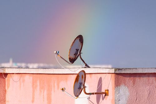 Free Two rusty satellite dishes on a rooftop against a vibrant rainbow in Tunisia. Stock Photo