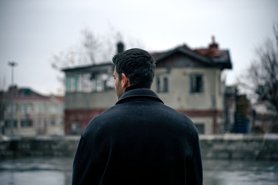 Adult man in winter coat stands in front of an old building in a snowy urban setting.
