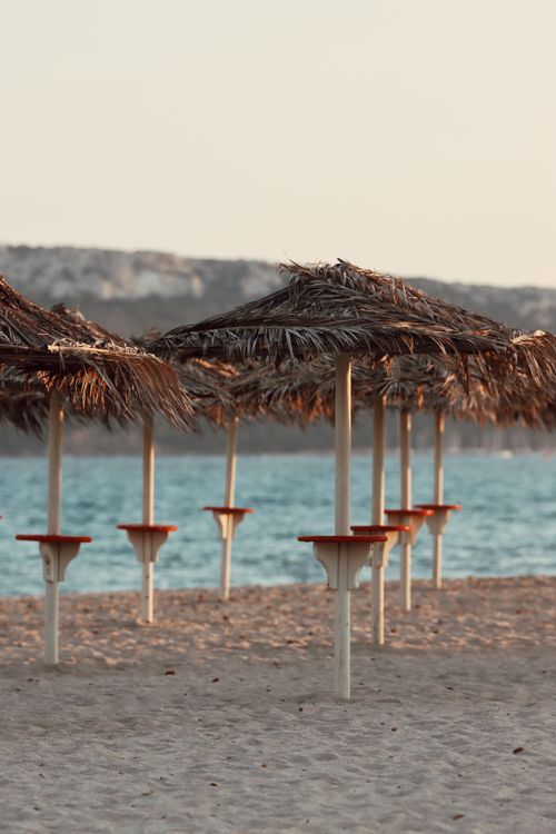 Free Peaceful beach with straw umbrellas by the azure sea in Sardinia, Italy, capturing the serene summer vibe. Stock Photo