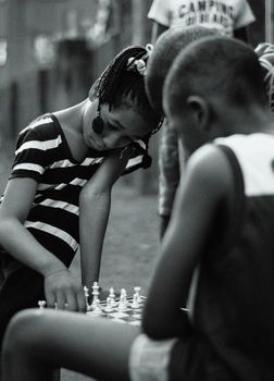 Young children engaged in a game of chess outside, captured in classic black and white.