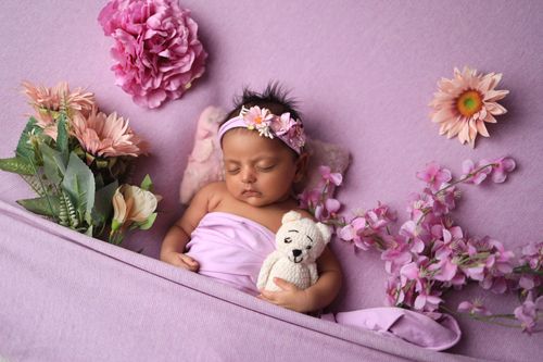 Free A serene photograph of a baby sleeping surrounded by beautiful pink flowers and a plush toy, creating a peaceful atmosphere. Stock Photo