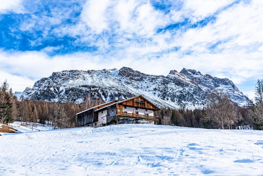 Scenic winter view of a rustic cabin in Cortina d'Ampezzo, Italy, with snowy mountains.