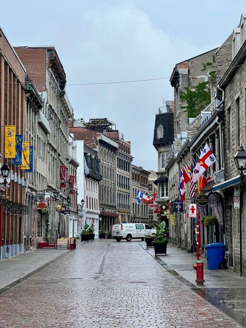 Free A picturesque view of a historic street in Old Quebec City, adorned with flags and wet cobblestones. Stock Photo