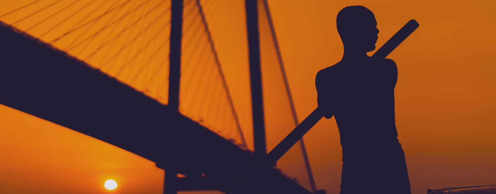 A striking silhouette of a man rowing at sunset near the iconic Howrah Bridge in Kolkata.