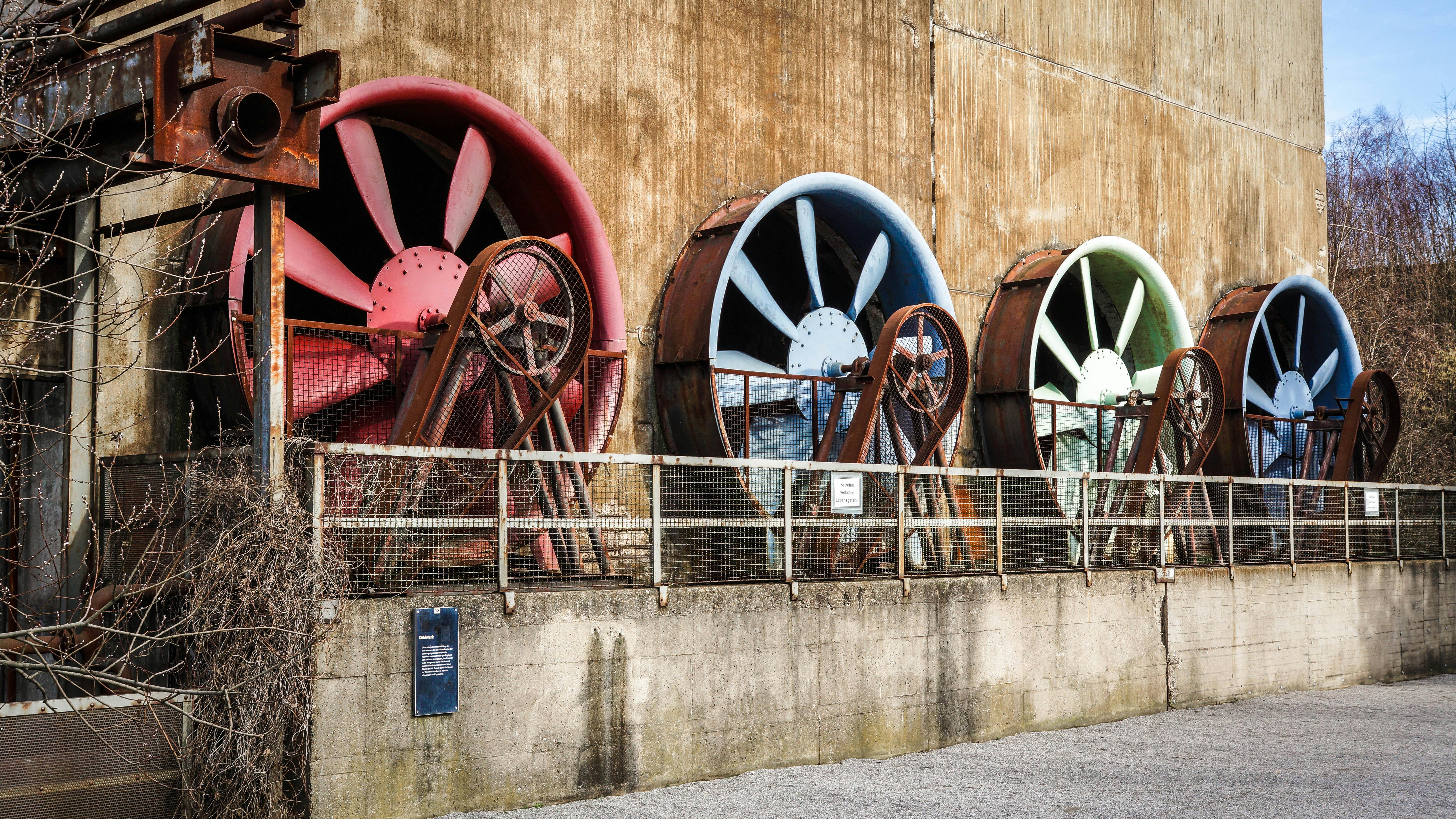 Fan & Aspiratör — A row of large colorful ventilation fans on a rustic industrial building exterior.