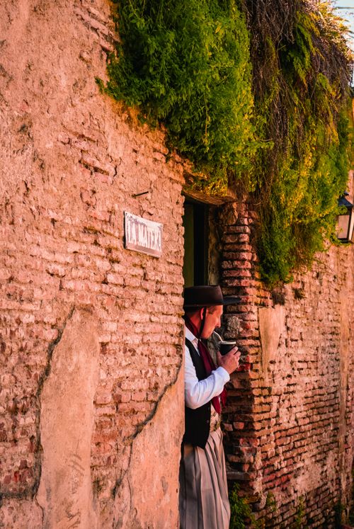 Free Man in traditional attire stands by an old brick building in a historic town street. Stock Photo
