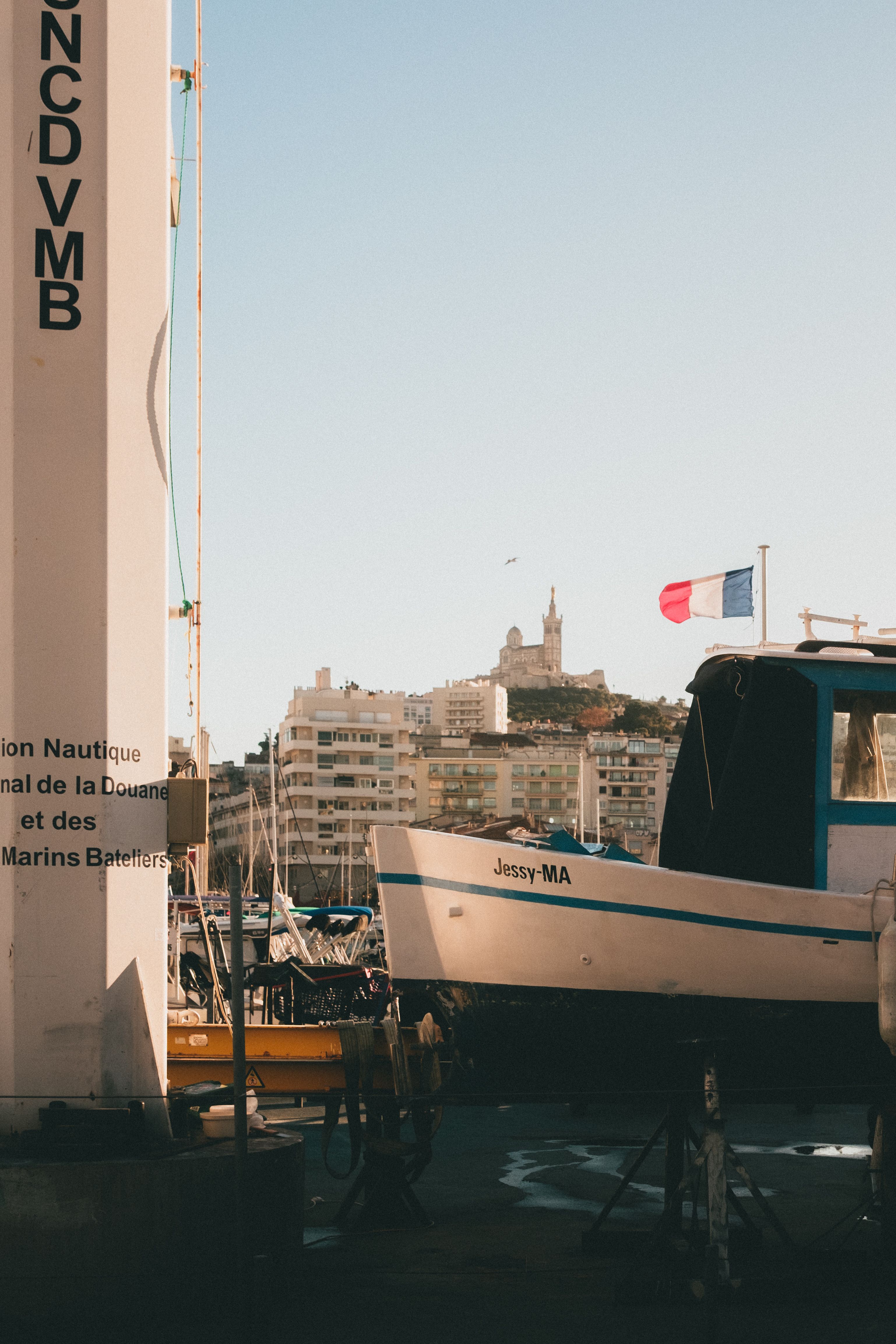 A vibrant view of Marseille harbor featuring the French flag and Notre-Dame de la Garde.