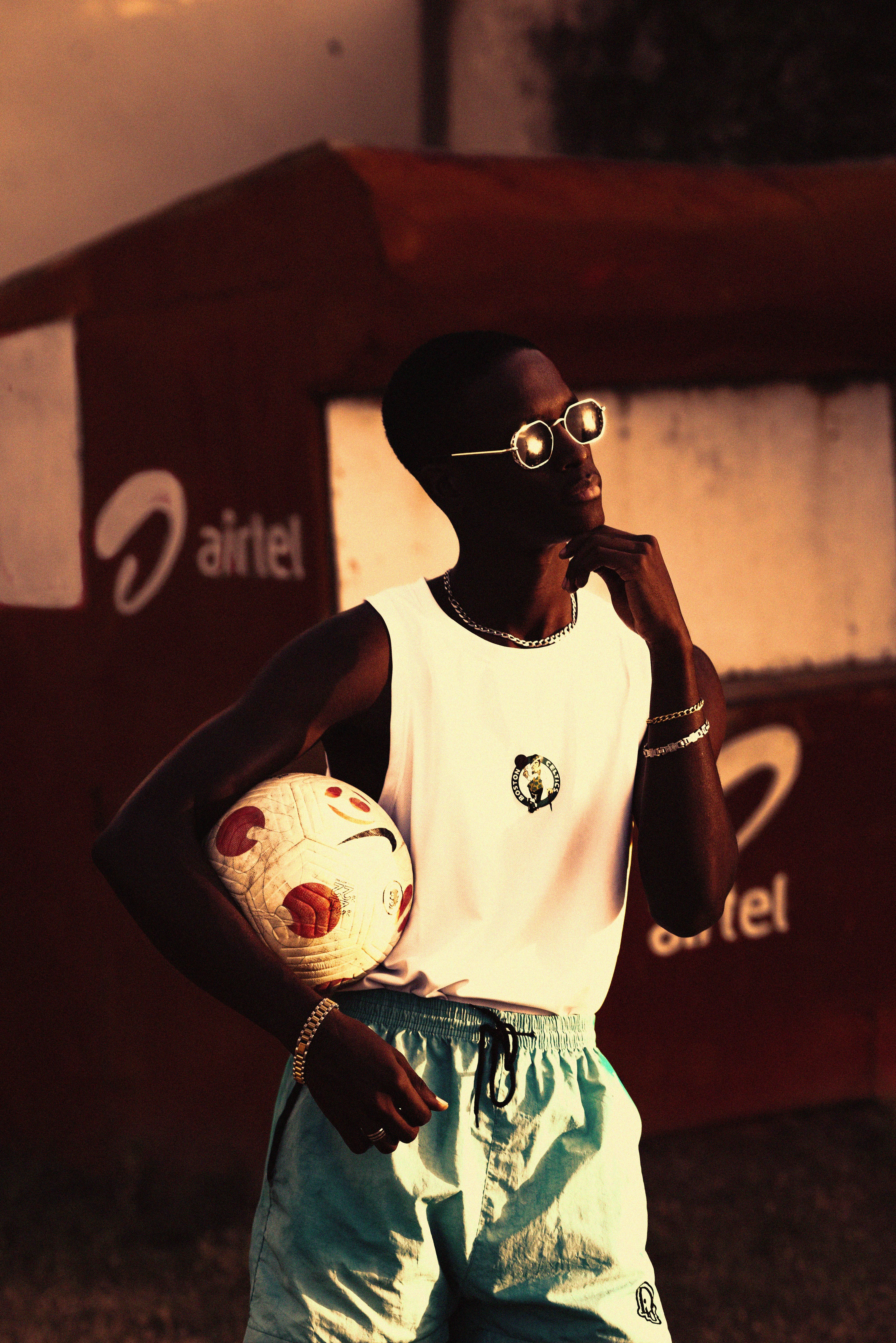 Stylish man holding a soccer ball, posing outdoors during sunset.