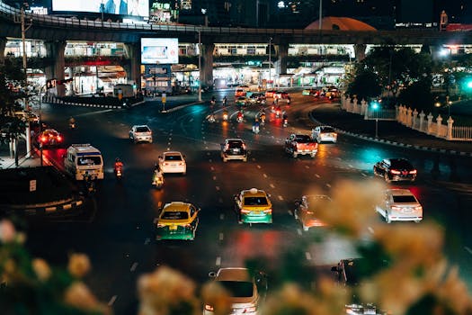 Dynamic night view of traffic on a bustling Bangkok street with taxis and motorbikes.