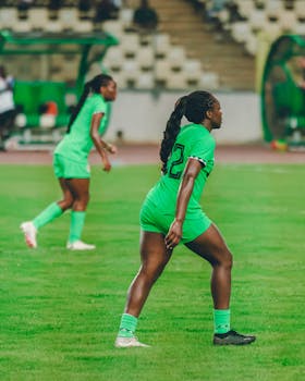 Women soccer players in action on the field, wearing green uniforms.