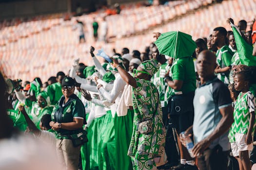 Energetic crowd of Nigerian sports fans wearing green, cheering during a stadium event.