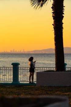 Silhouette of a woman by the sea at sunset with a distant city skyline.