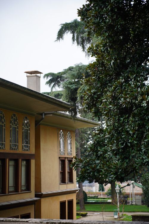 Free View of a historic building exterior with decorative windows and a lush garden setting. Stock Photo