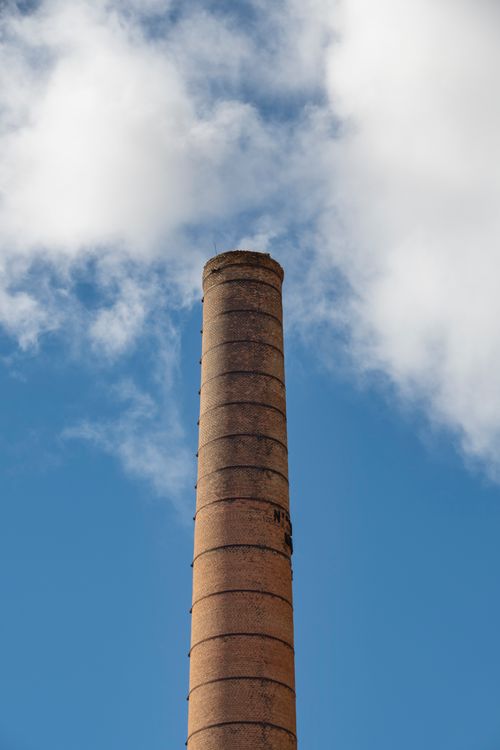 Free A tall brick chimney reaching up against a backdrop of blue sky and fluffy clouds. Stock Photo