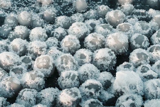 Frozen ice spheres covered in snow on a winter lake, showcasing natural patterns.