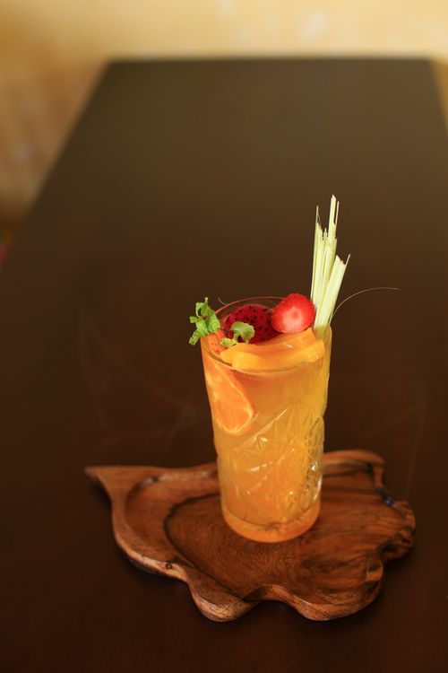Free A vibrant tropical drink in Hoi An, Vietnam, featuring orange slices and lemongrass garnish, served on a wooden platter. Stock Photo