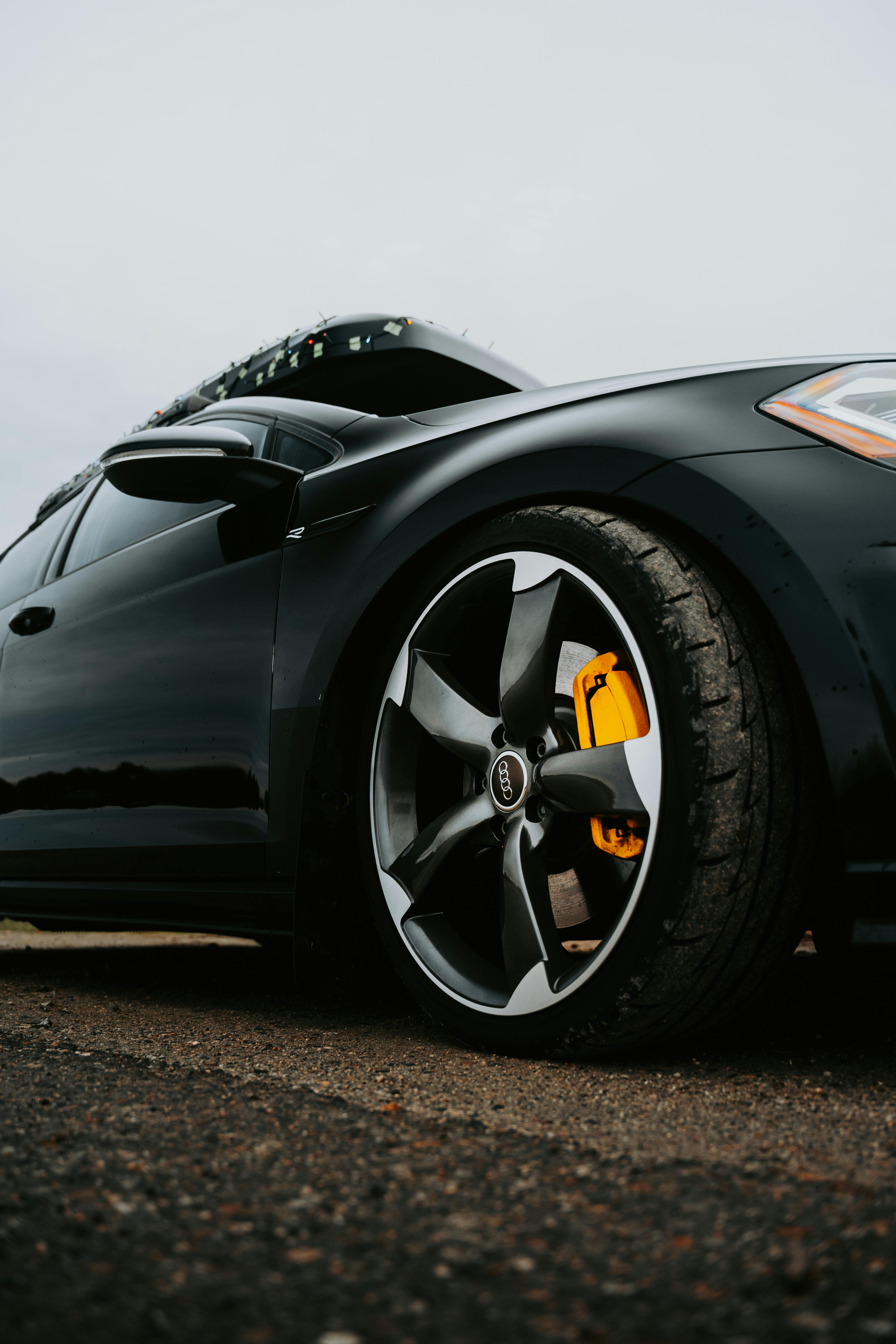 Close-up view of a stylish black car wheel and tire on an asphalt road with open hood.