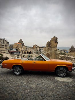 Classic orange convertible car parked in Cappadocia, Turkey, against unique rock formations.