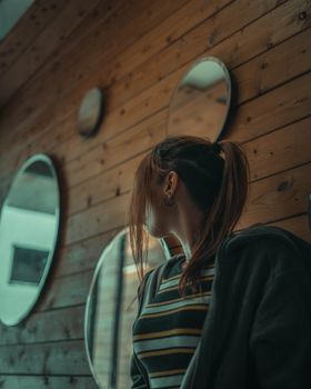 A woman in a cozy room with wooden paneling and circular mirrors.