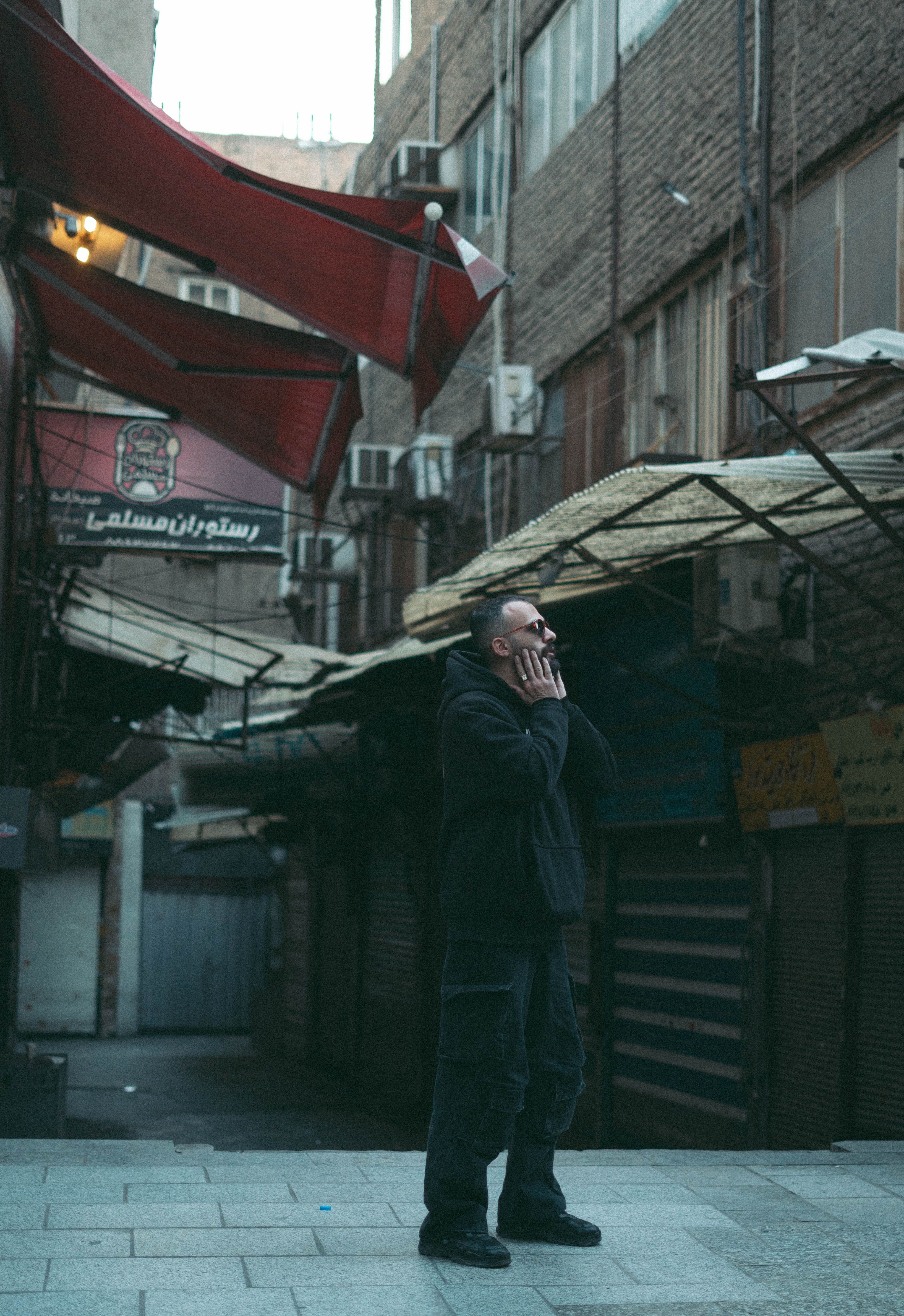 A contemplative man stands in a dimly lit urban alleyway with artistic signage.