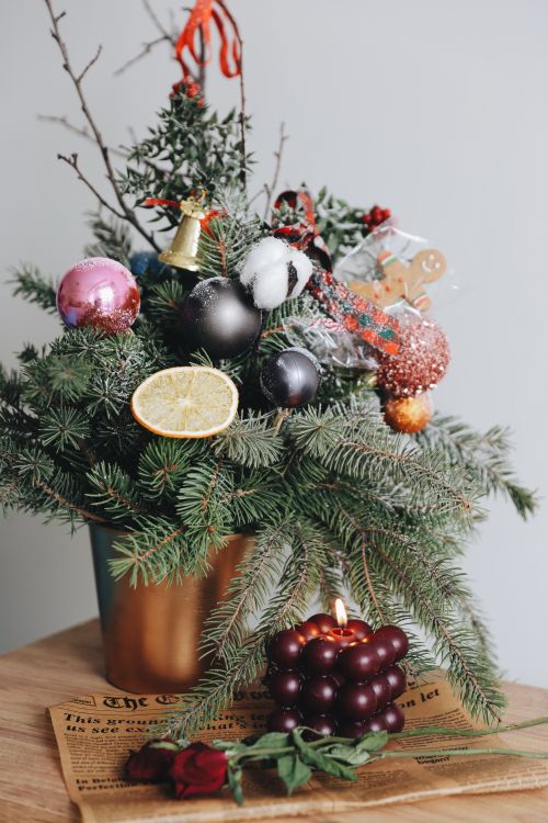 Free A Christmas floral arrangement with evergreen branches, ornaments, and a burning candle set on a wooden table. Stock Photo