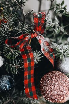 Close-up of a snowy Christmas tree decorated with a red plaid ribbon and ornaments, creating a festive winter scene.