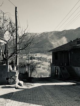 Monochrome image of a rustic village road leading to mountains, exuding timeless charm.