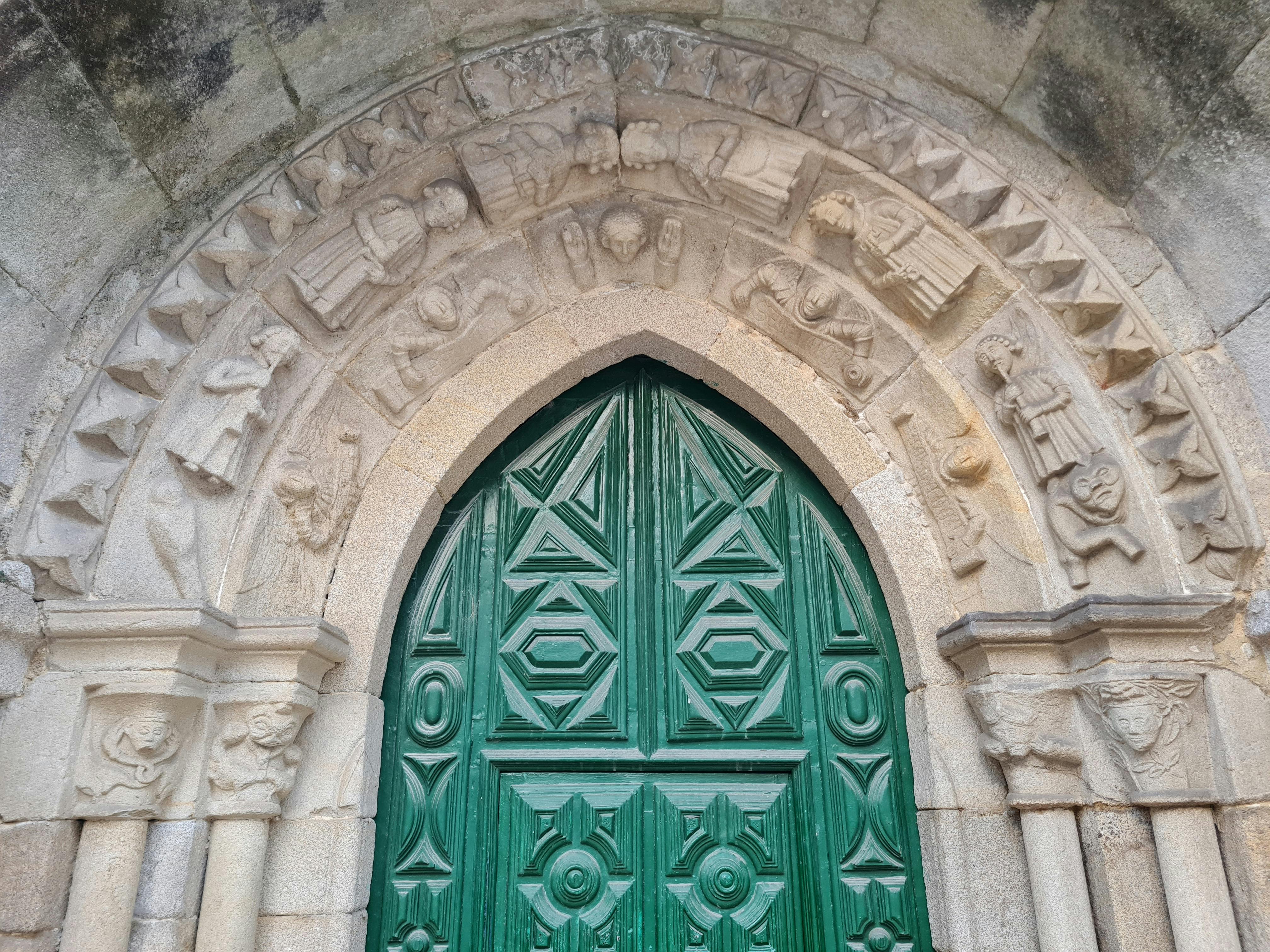 Antique stone archway with intricate carvings framing a green wooden door.