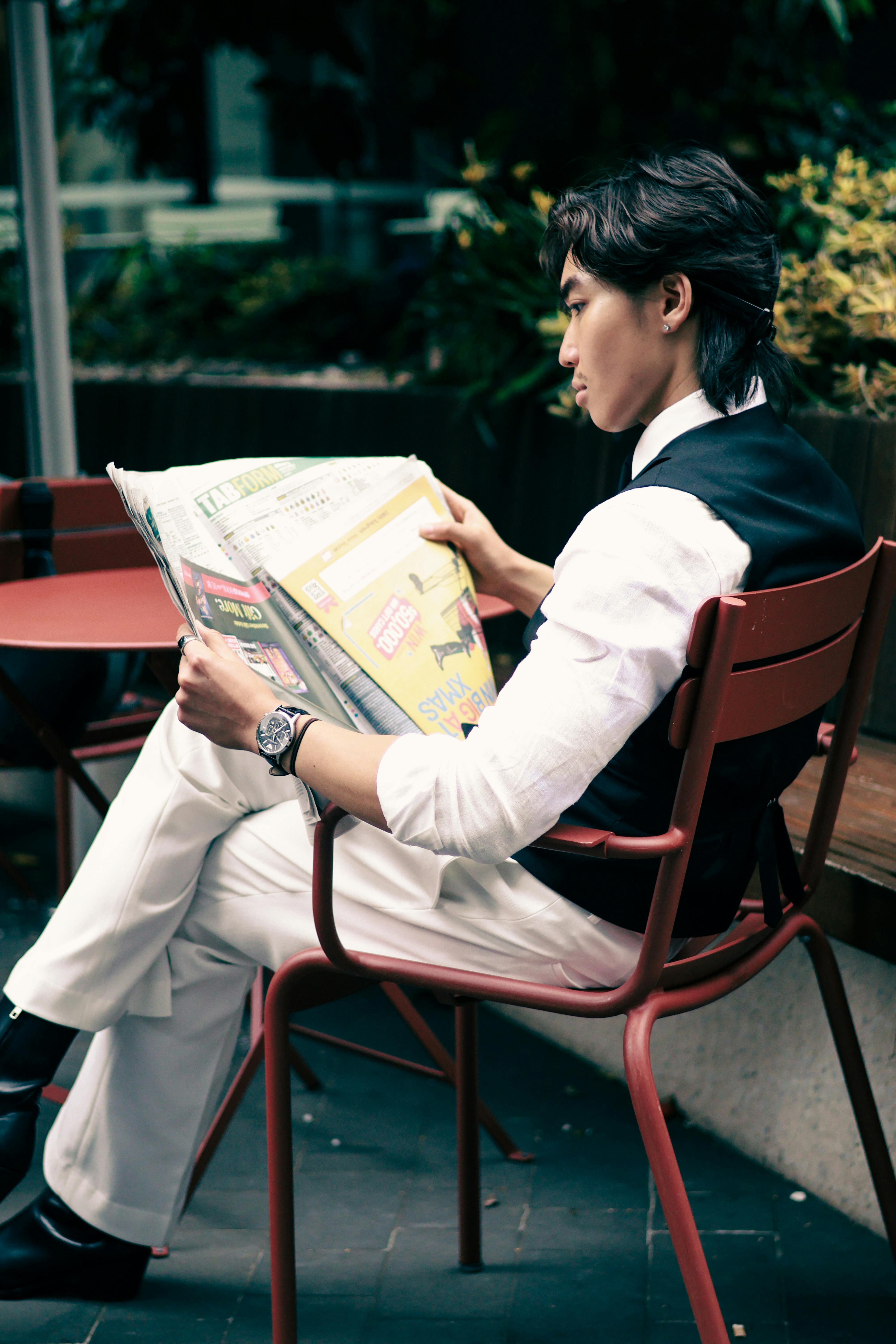 Gratis Un uomo elegante che legge il giornale in un bar all'aperto, trasudando raffinatezza. Foto a disposizione