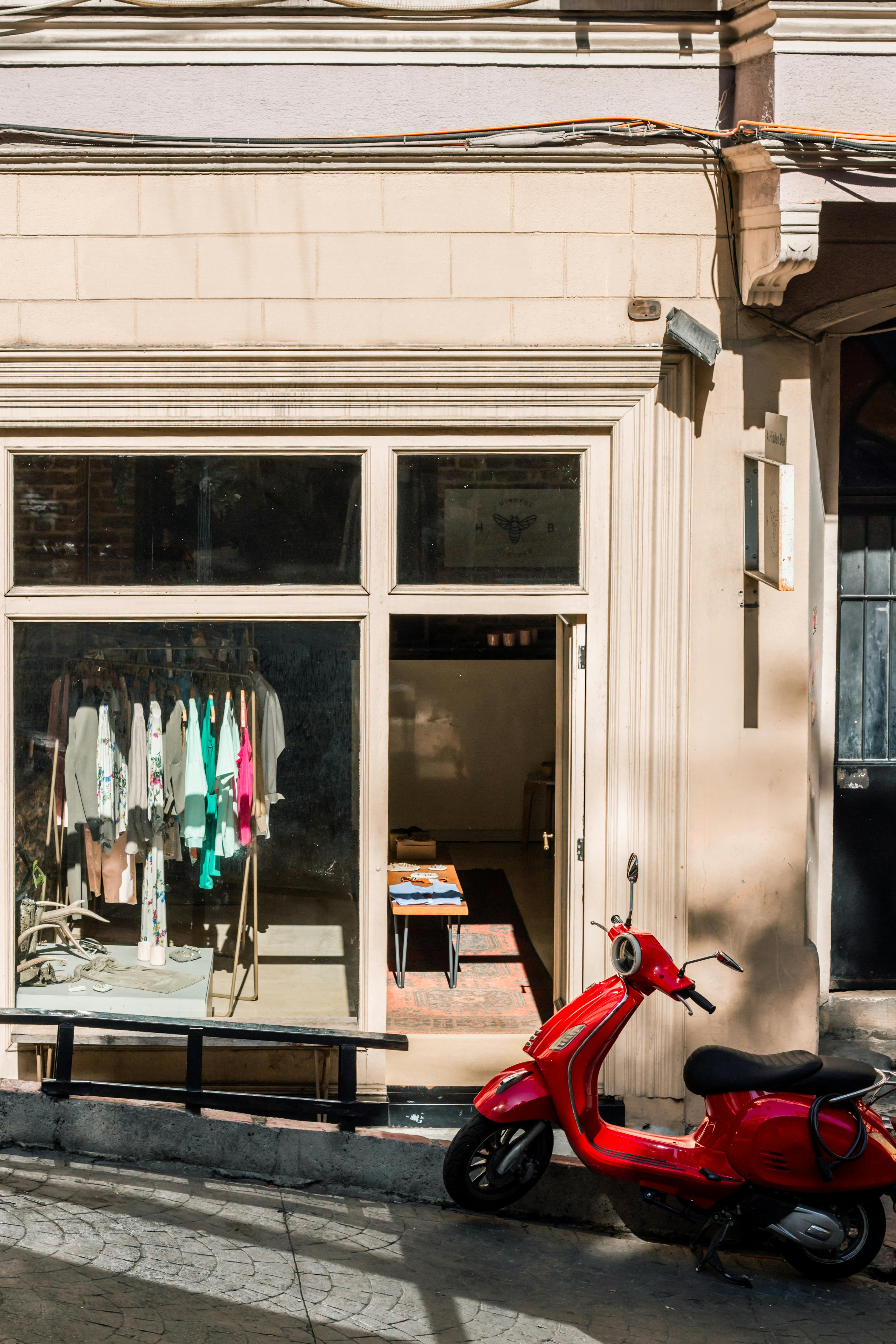 Bright storefront with vibrant clothing display and a classic red scooter parked in sunlight.