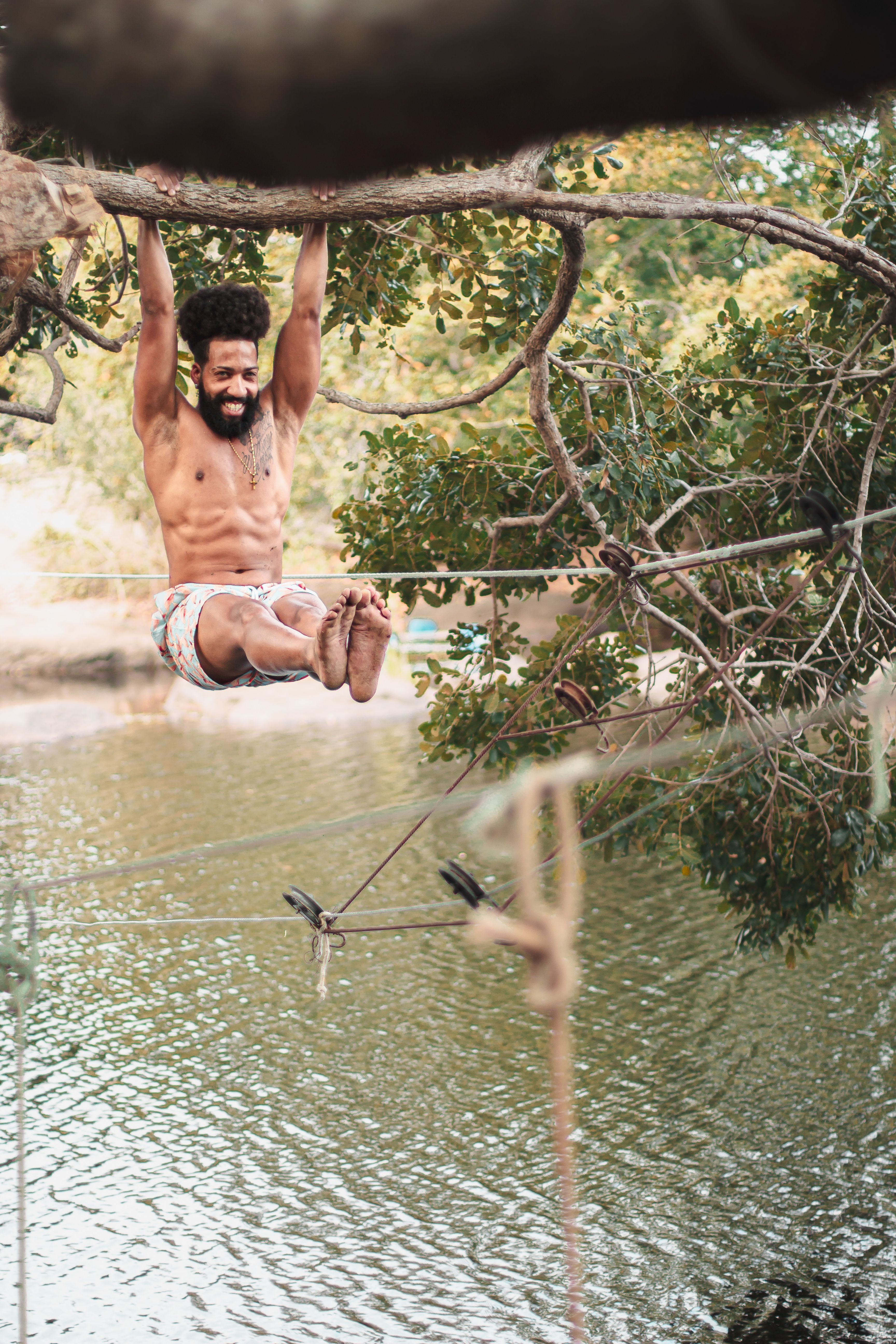 A man enjoying an outdoor adventure, swinging on a tree above a river.