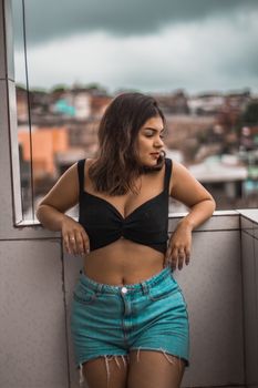 Confident woman in casual summer outfit relaxing on a city balcony.