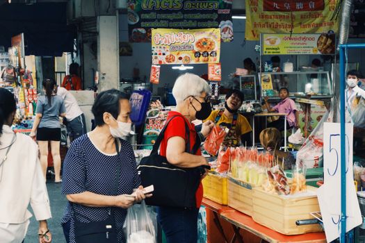 Colorful street market with vendors and shoppers wearing masks in bustling outdoor setting.